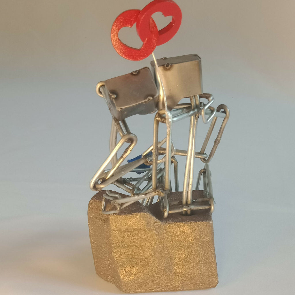 Sculpture en fils d’acier sur socle doré, couple et cœur rouge, angle rapproché