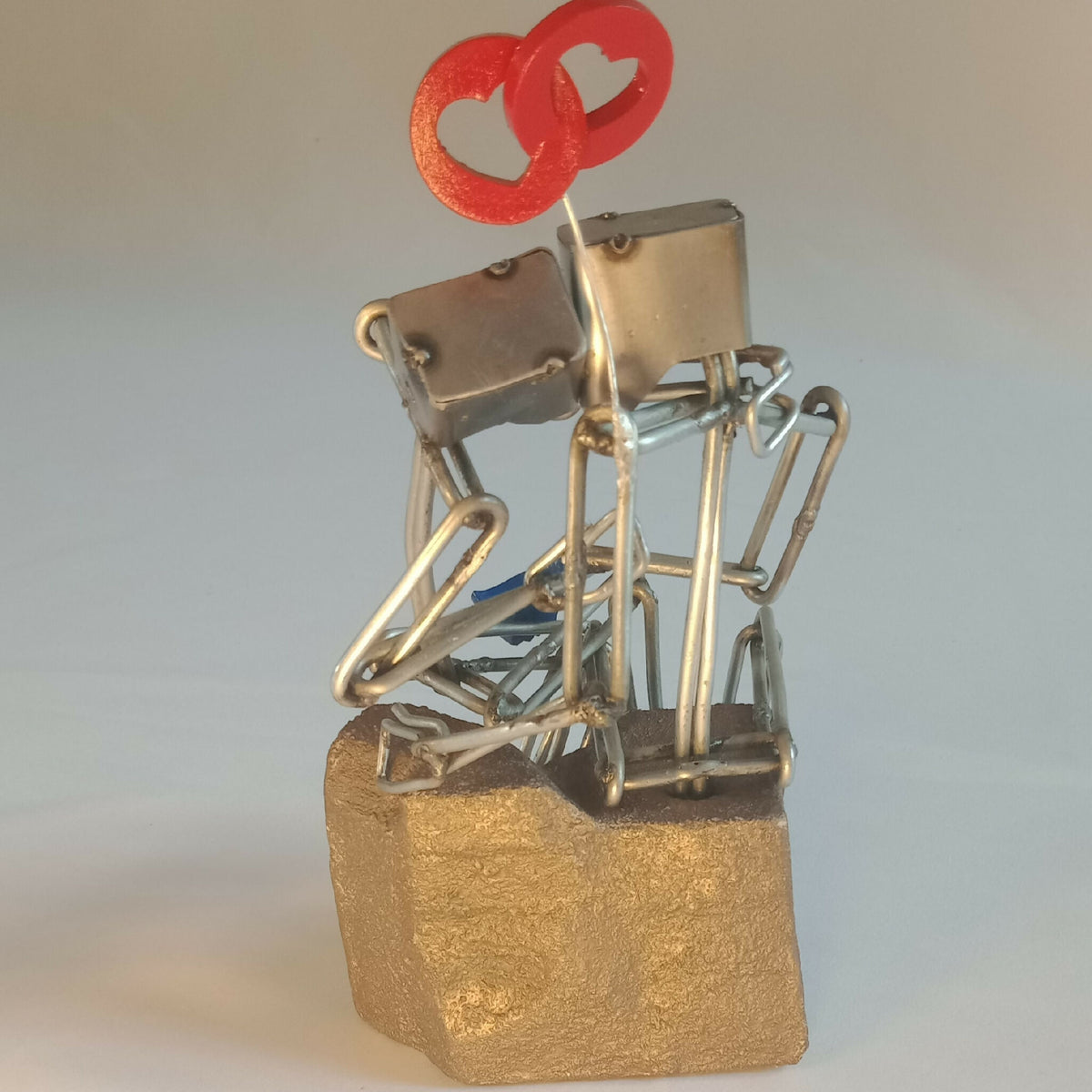 Sculpture en fils d’acier sur socle doré, couple et cœur rouge, angle rapproché
