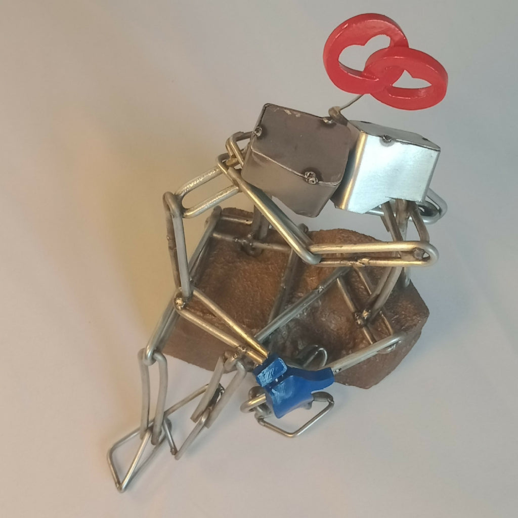 Sculpture en fils d’acier sur socle, couple enlacé, cœur rouge en haut et assise bleue