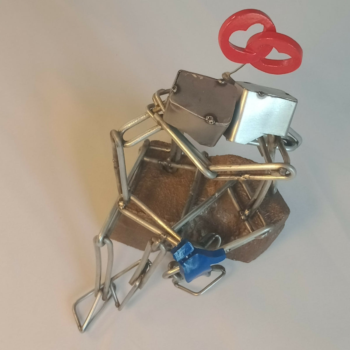 Sculpture en fils d’acier sur socle, couple enlacé, cœur rouge en haut et assise bleue