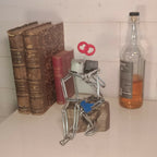 Sculpture en fils d’acier sur socle doré, avec cœur rouge et assise bleue, en vitrine