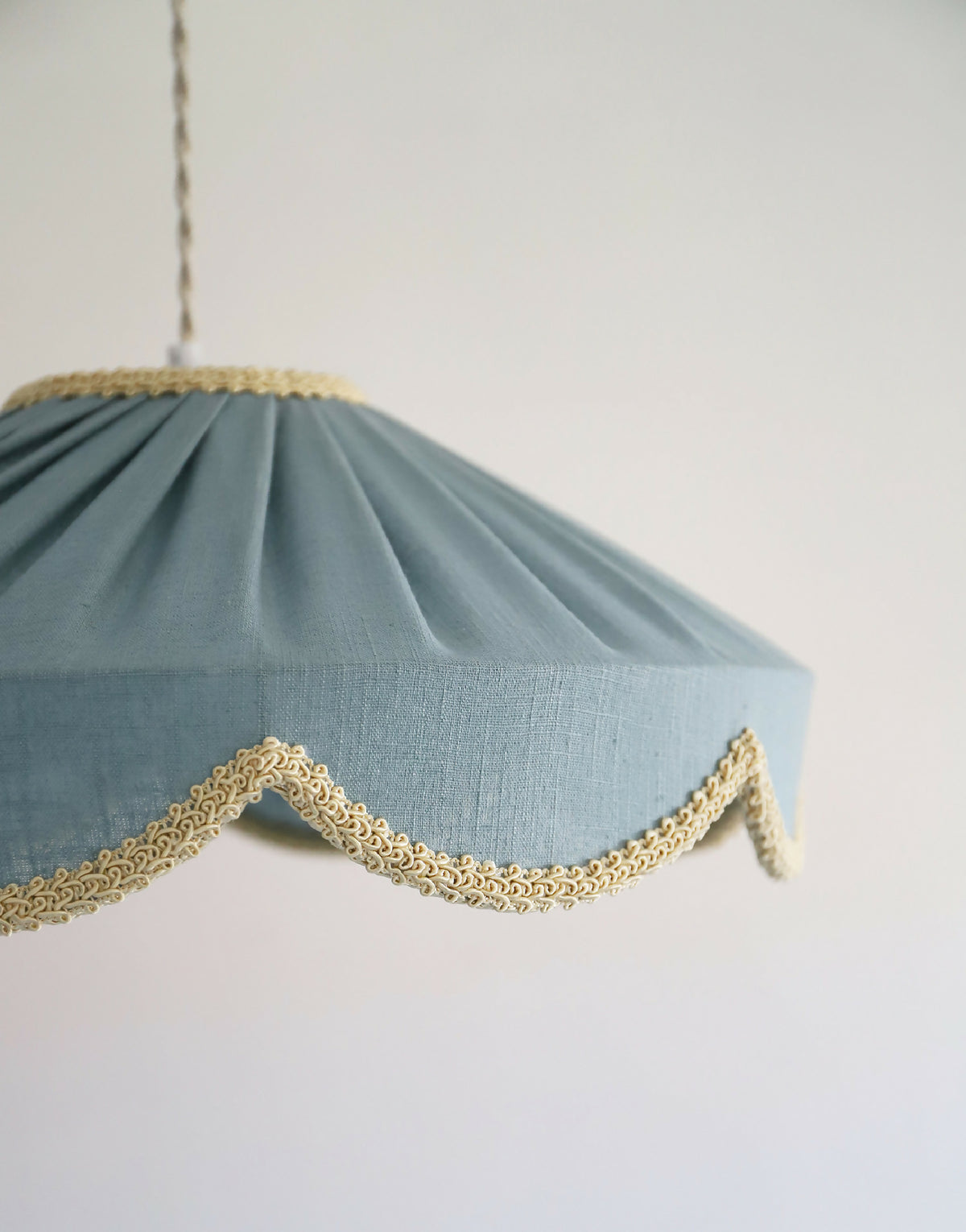 Suspension en tissu bleu minéral, gros plan sur liseré doré ondulé sur le bord