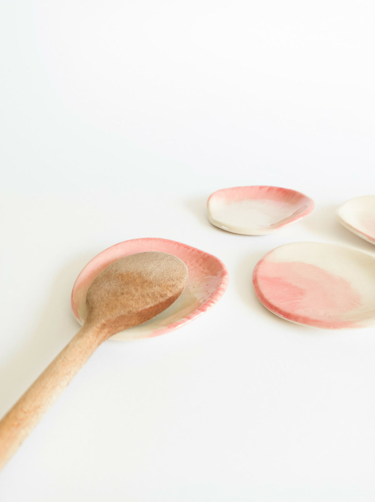 Repose-cuillère ovale en grès, dégradé rose pâle sur beige, avec cuillère en bois