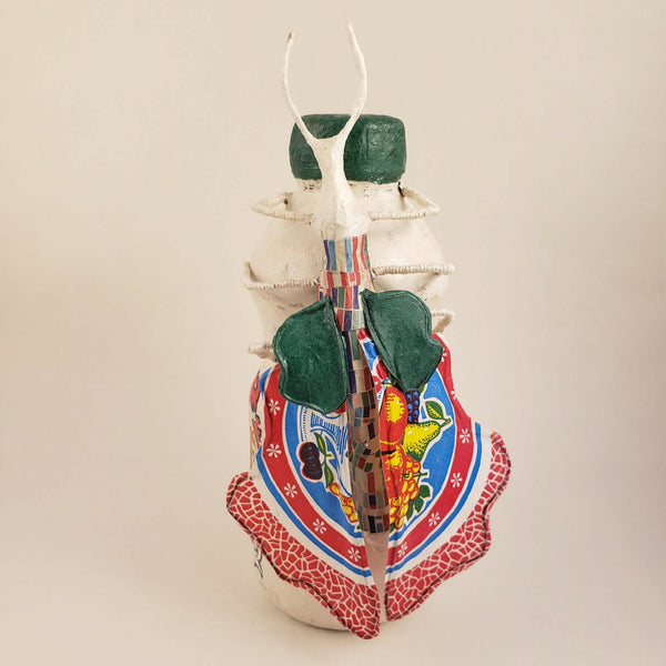 Sculpture posée sur une bouteille, corps blanc, capuchon vert, tablier rouge et décor multicolore
