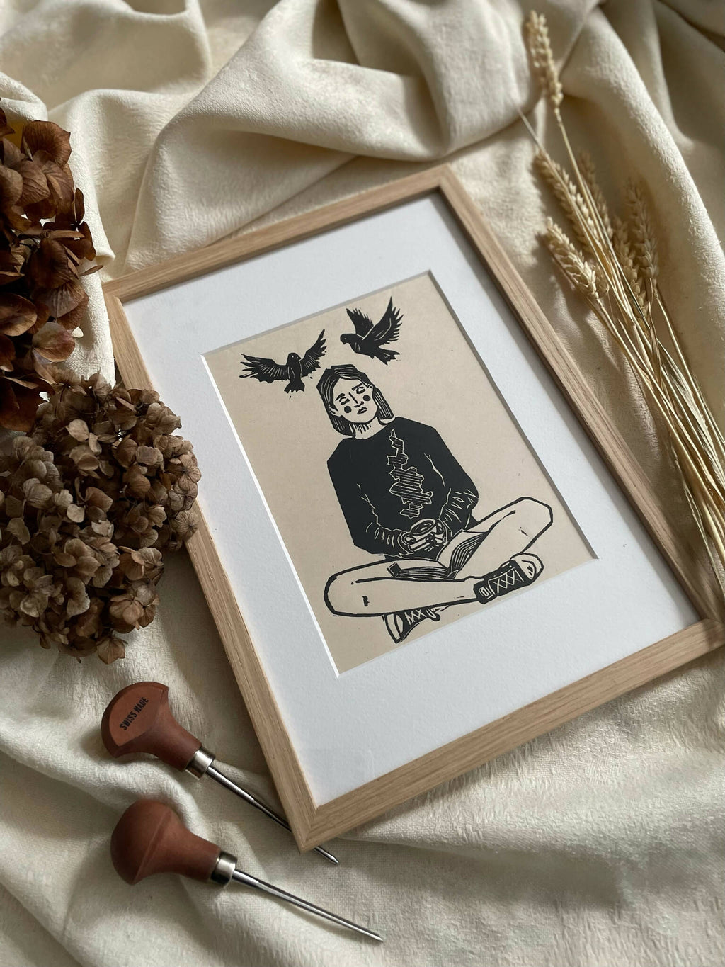 Illustration encadrée bois clair : femme assise, oiseaux aux ailes déployées au-dessus.