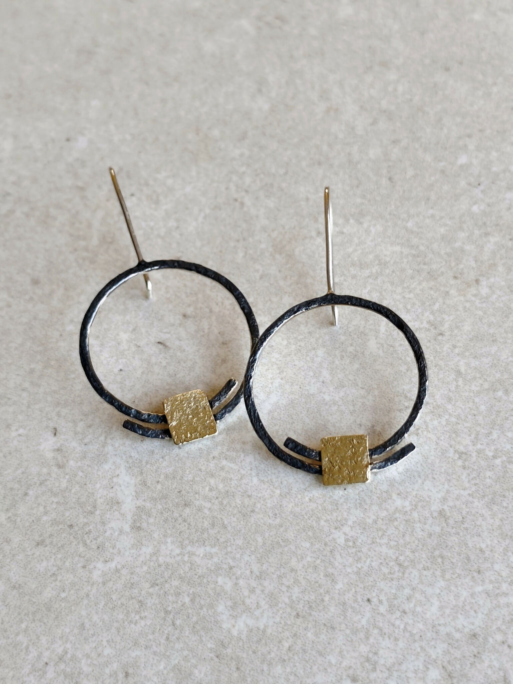 Boucles d’oreilles pendantes : deux anneaux noirs avec carrés dorés texturés, tiges argentées.