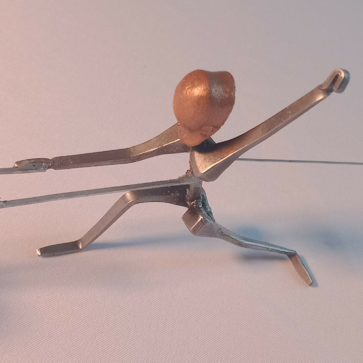 Figurine d’escrimeuse en acier, posture allongée, tête cuivre et poignée de fleuret levée.