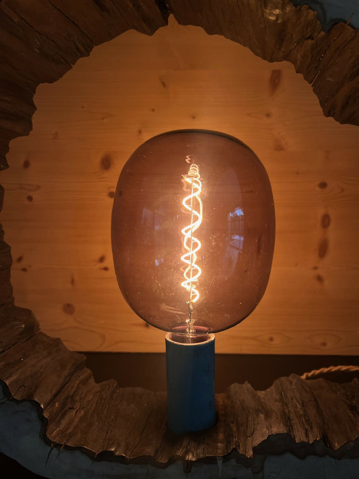 Sculpture lumineuse ronde avec ampoule fumée éclairée, enserrée dans un bord bois sombre