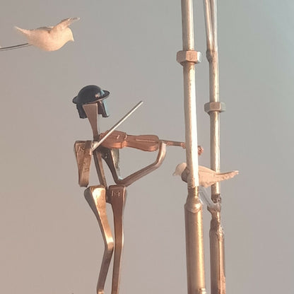 Musicien en métal doré avec instrument, sur manège décoratif, oiseaux en arrière-plan.