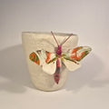 Sculpture de papillon multicolore sur pot en béton clair, ailes écartées