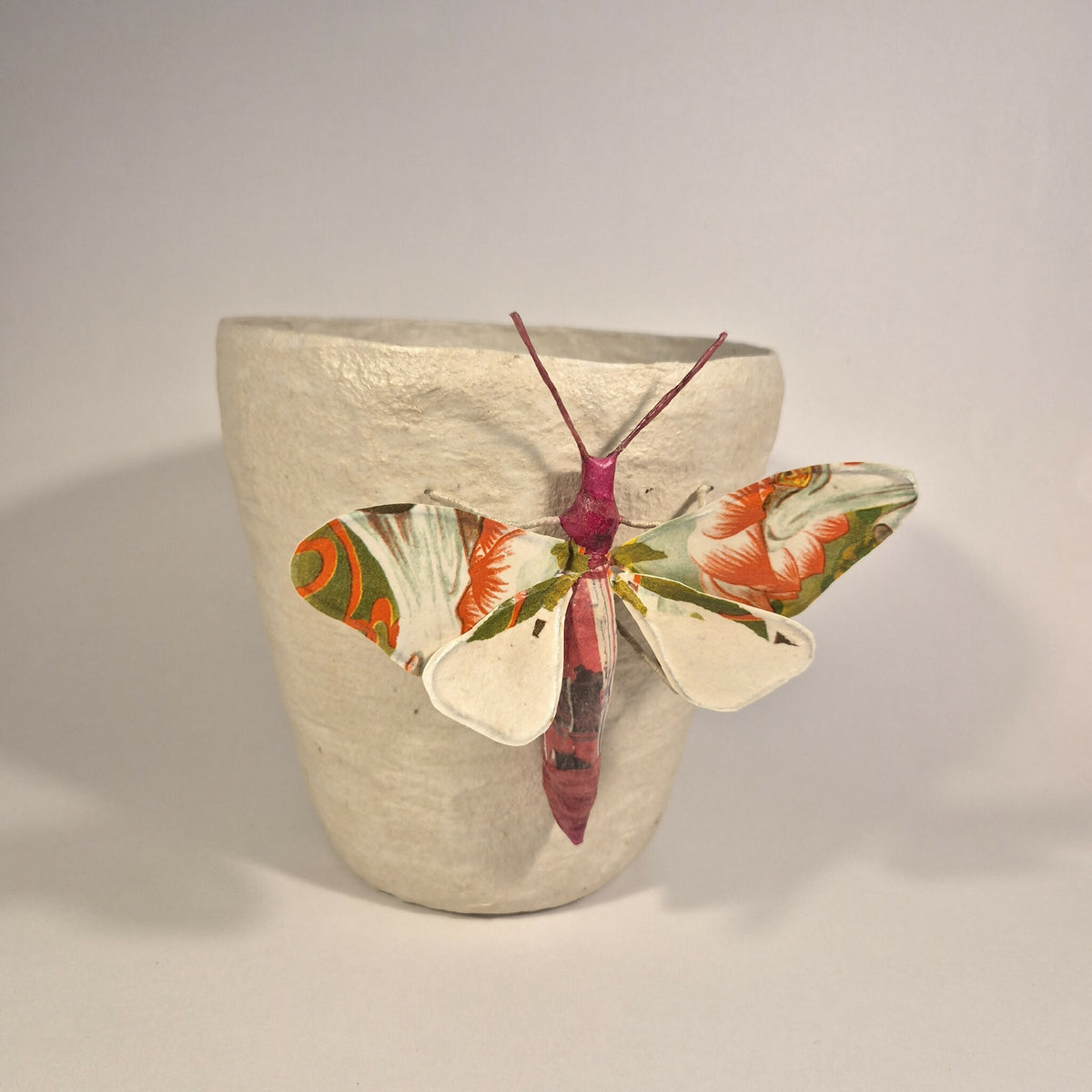 Sculpture de papillon multicolore sur pot en béton clair, ailes écartées