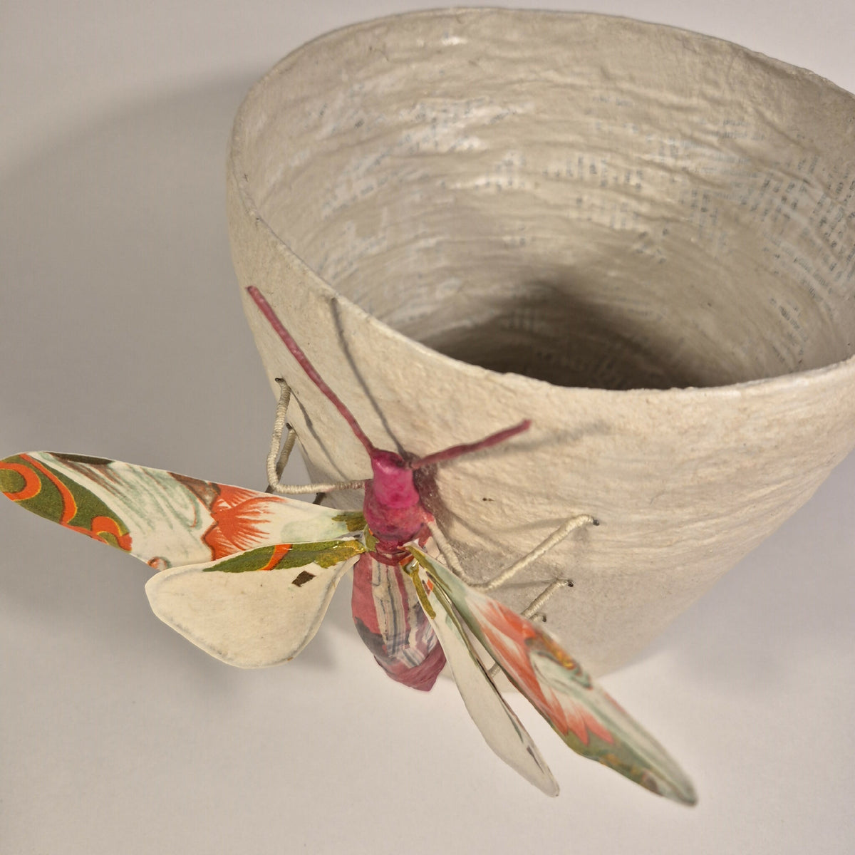 Sculpture de papillon multicolore fixée sur pot en béton clair, ouverture visible