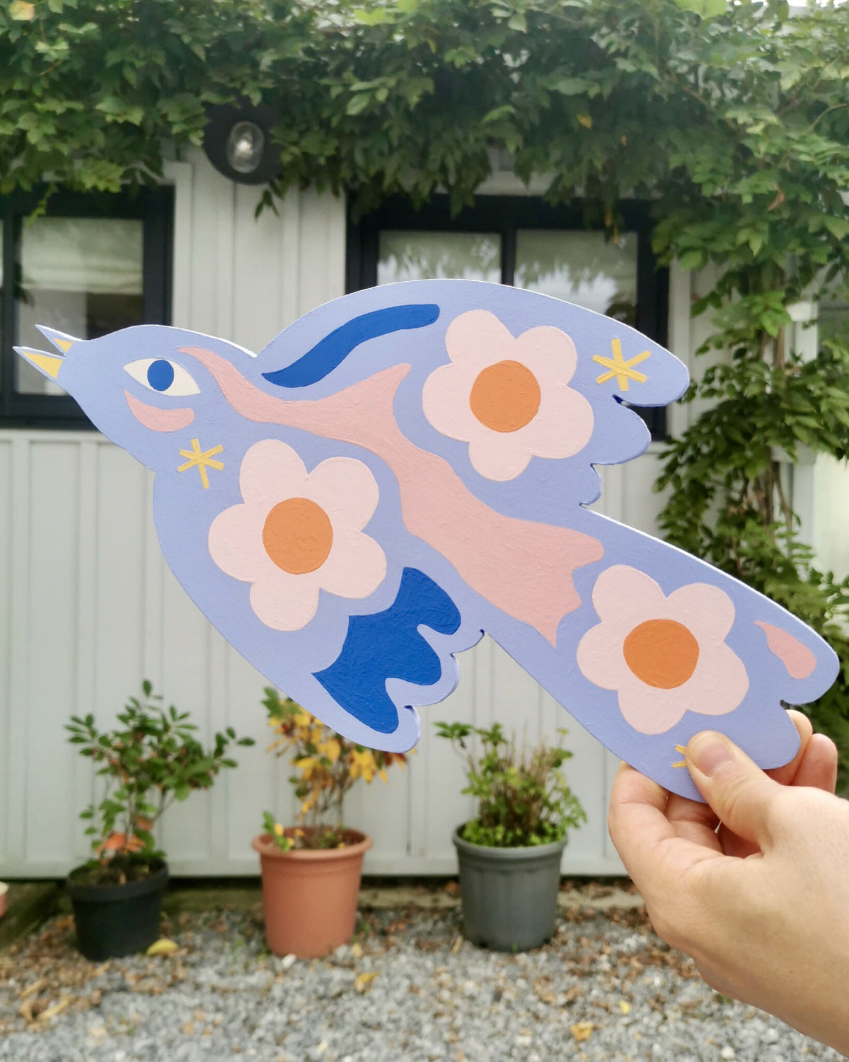 Oiseau en bois bleu clair décoré de fleurs orange et étoiles jaunes, vue main