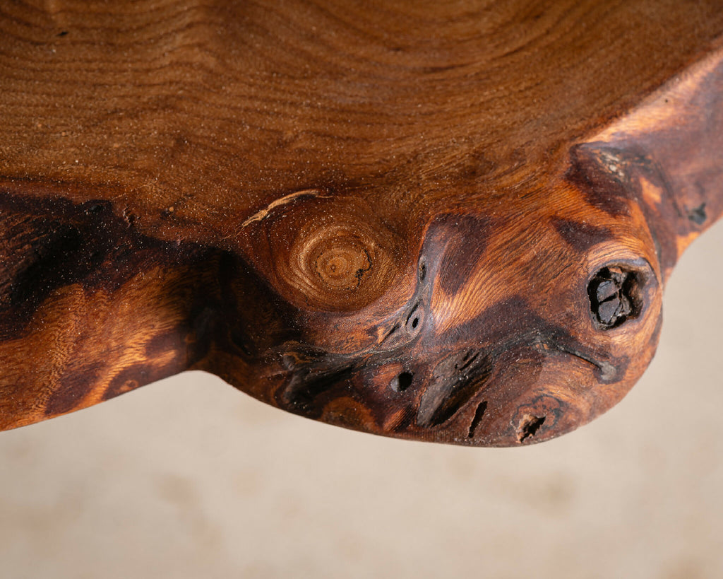 Table en bois massif, détail sculpté avec nœud et textures sombres du bois.