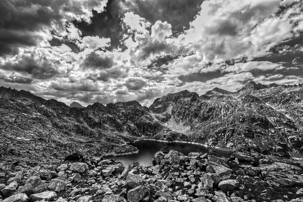 Lac de Migouélou, eau calme entourée de montagnes rocheuses et ciel nuageux