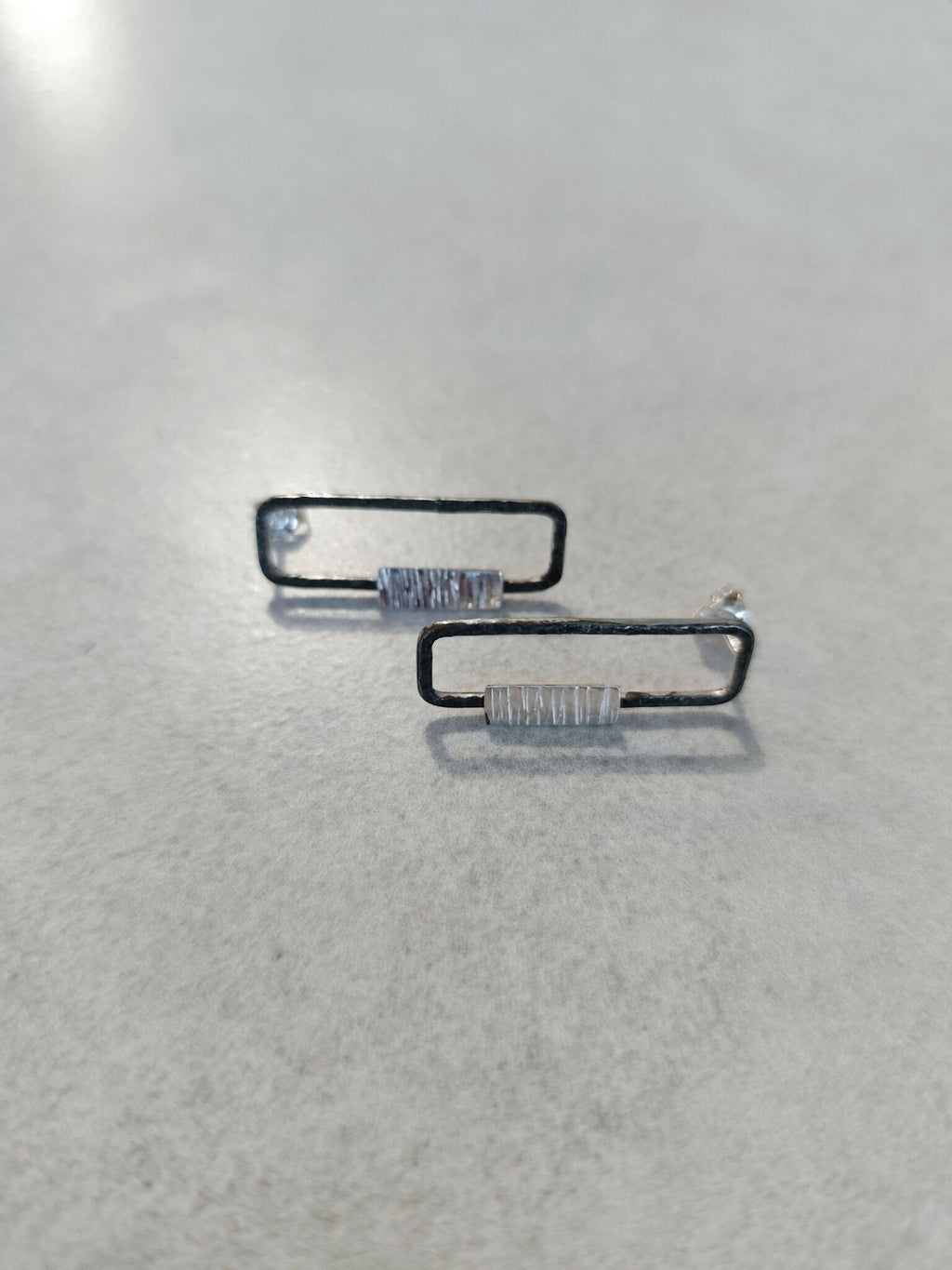 Boucles d’oreilles rectangulaires, plaquettes striées et reflets argentés, vue rapprochée