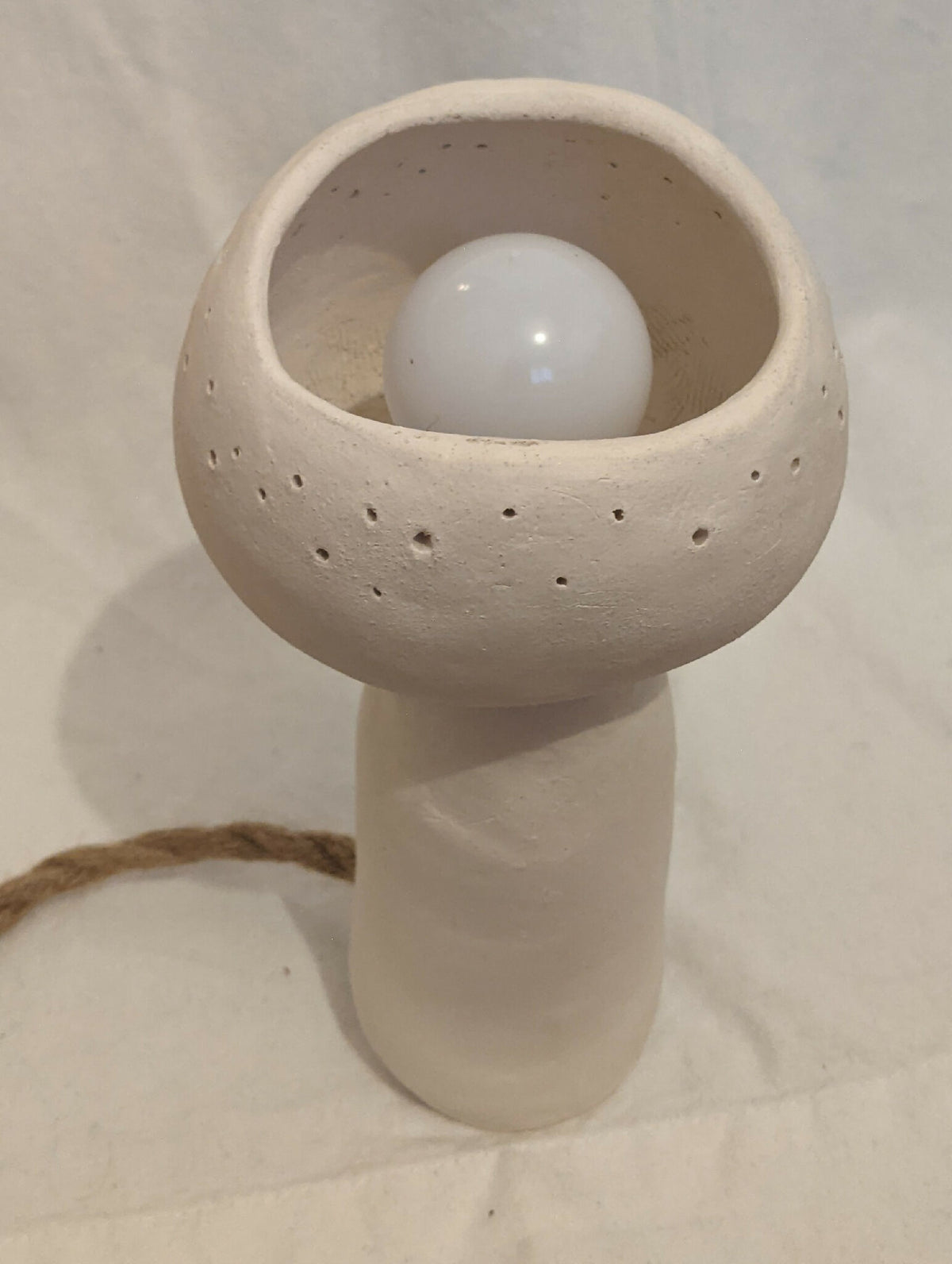 Lampe à poser champignon en céramique blanc cassé, globe lumineux visible à l’intérieur.