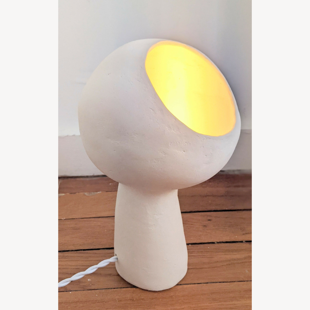 Lampe à poser design blanche, abat-jour rond, lumière chaude allumée, câble à la base