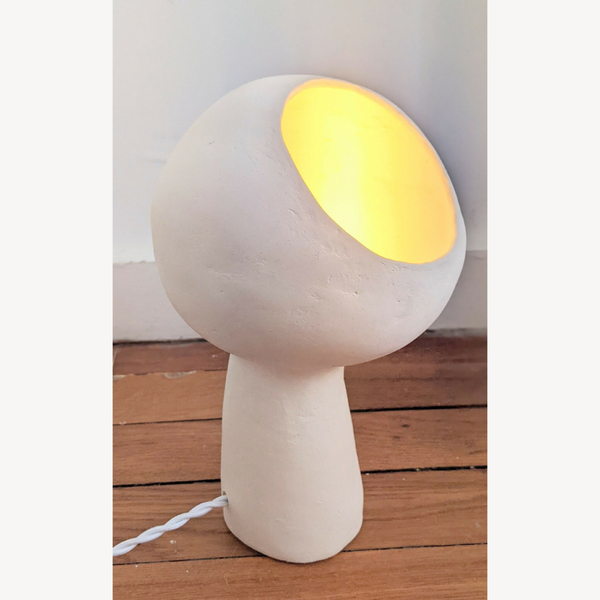 Lampe à poser design blanche, abat-jour rond, lumière chaude allumée, câble à la base