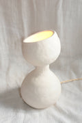 Lampe design blanche en forme de sablier, allumée, câble visible