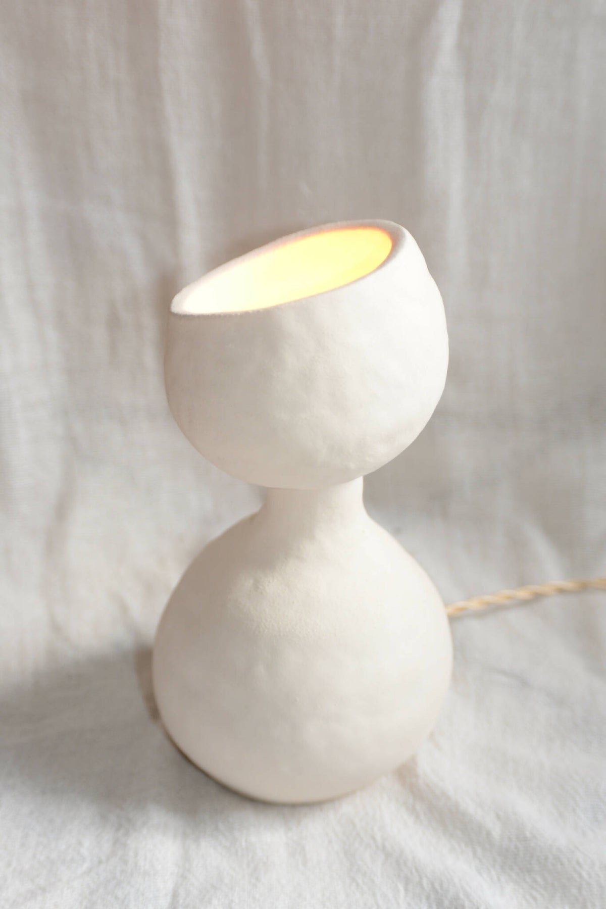 Lampe design blanche en forme de sablier, allumée, câble visible