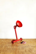 Lampe rouge sur trépied, abat-jour conique et cordon spiralé au sol