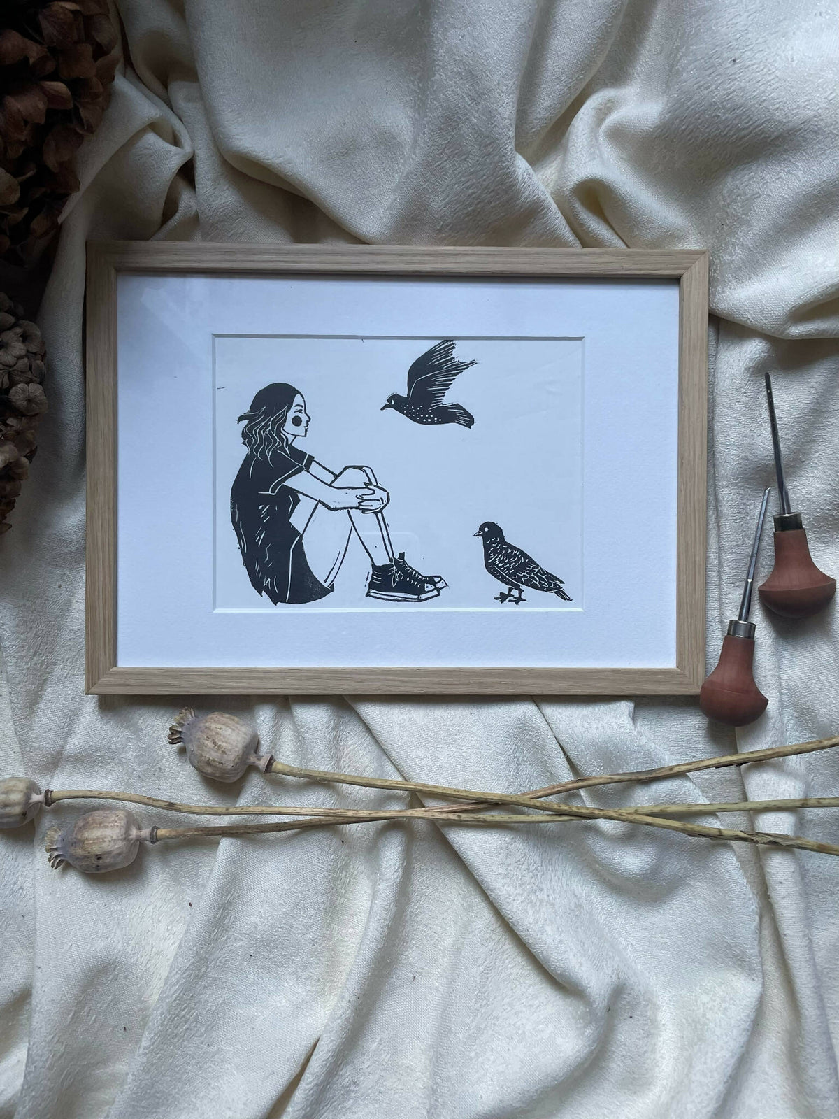 Cadre en bois clair avec affiche de jeune fille et oiseaux noirs sur fond clair