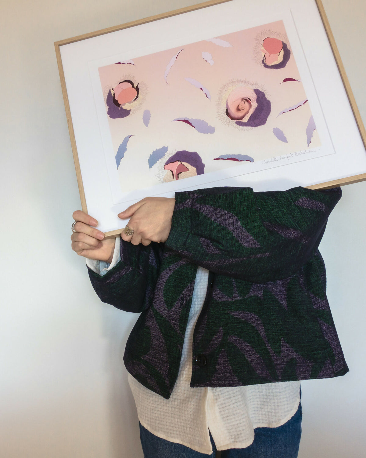 Affiche encadrée tenue par une personne, motif pastel de plumes et soleils