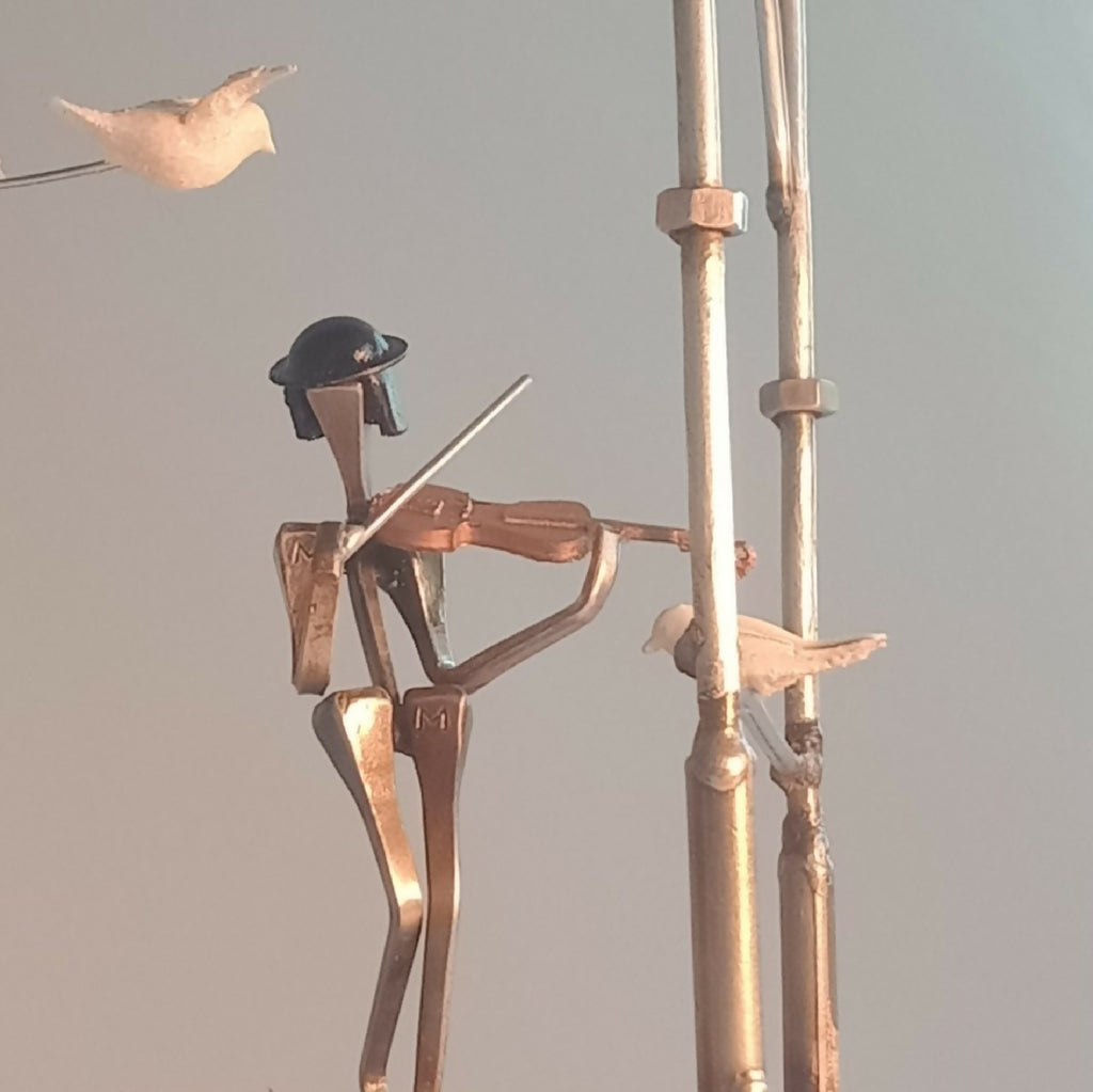 Musicien en métal doré avec instrument, sur manège décoratif, oiseaux en arrière-plan.