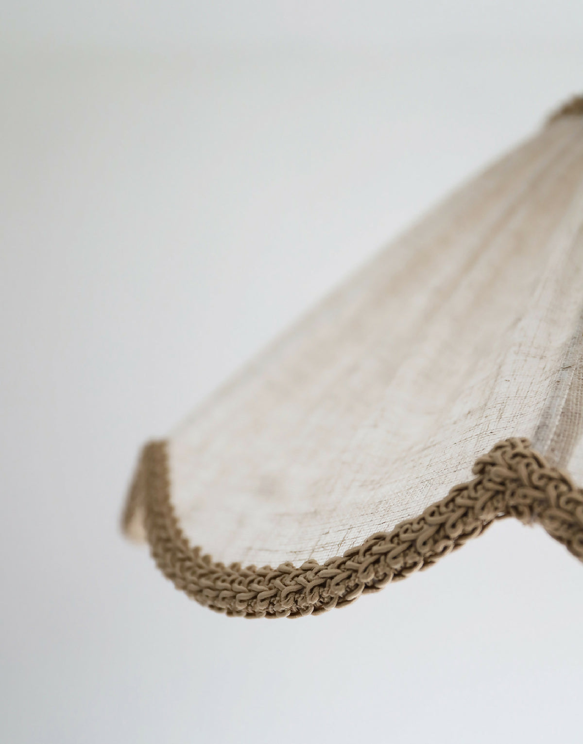 Détail de l’abat-jour beige : tissu texturé et bord ondulé tressé