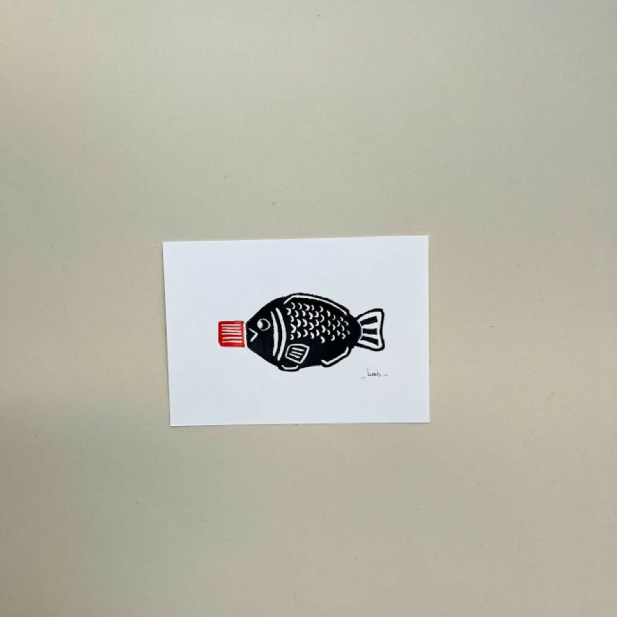 Linogravure A6 10×15 cm : poisson noir et étiquette rouge, sur fond blanc.