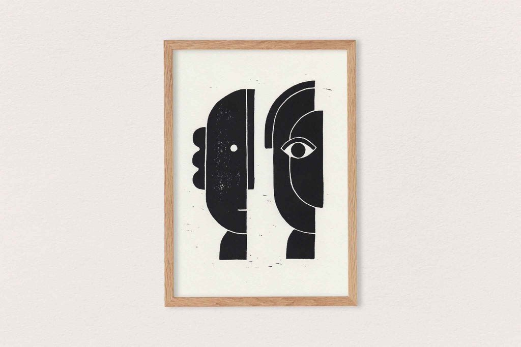 Linogravure encadrée : visages abstraits noirs, lignes blanches, fond clair.