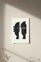 Linogravure encadrée, visages abstraits noirs sur fond clair.