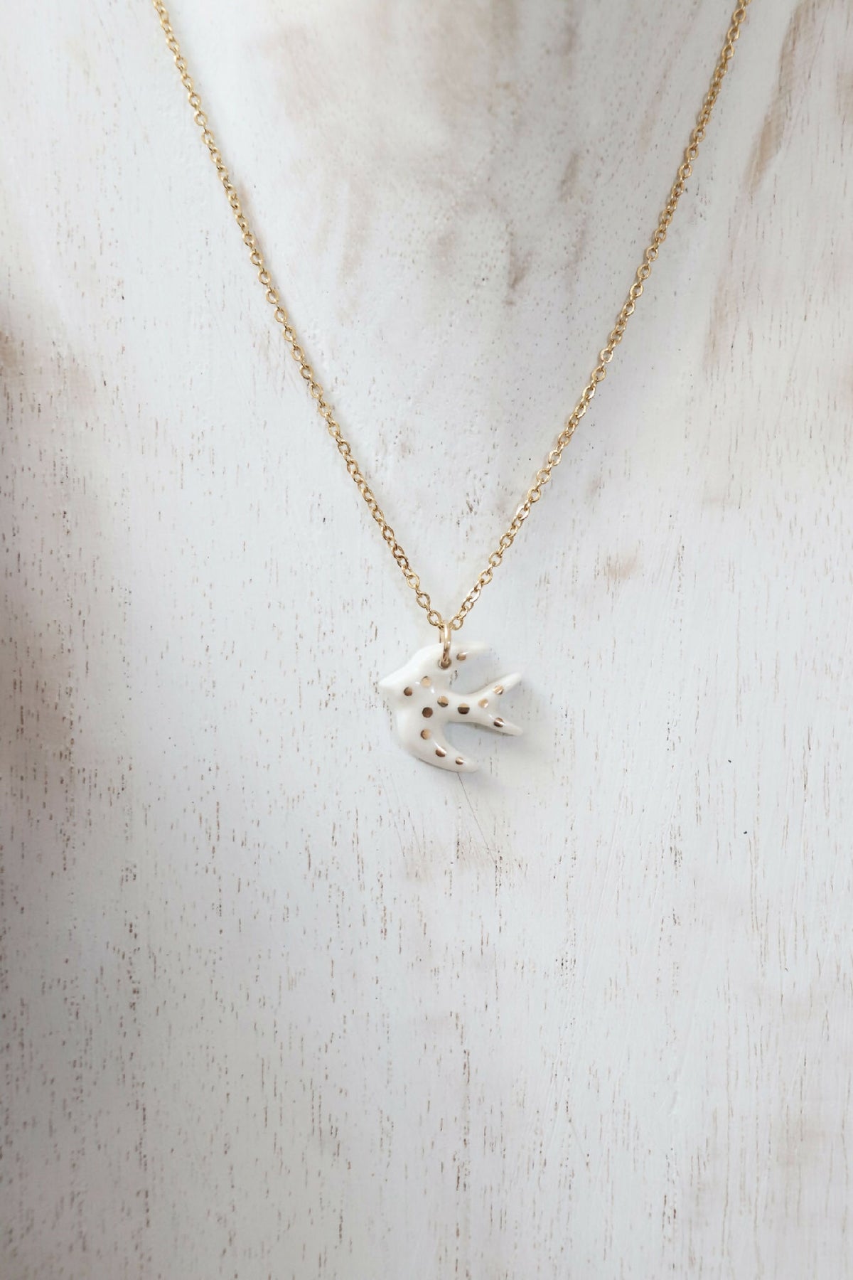 Collier à pendentif hirondelle en porcelaine blanche, chaîne dorée allongée.