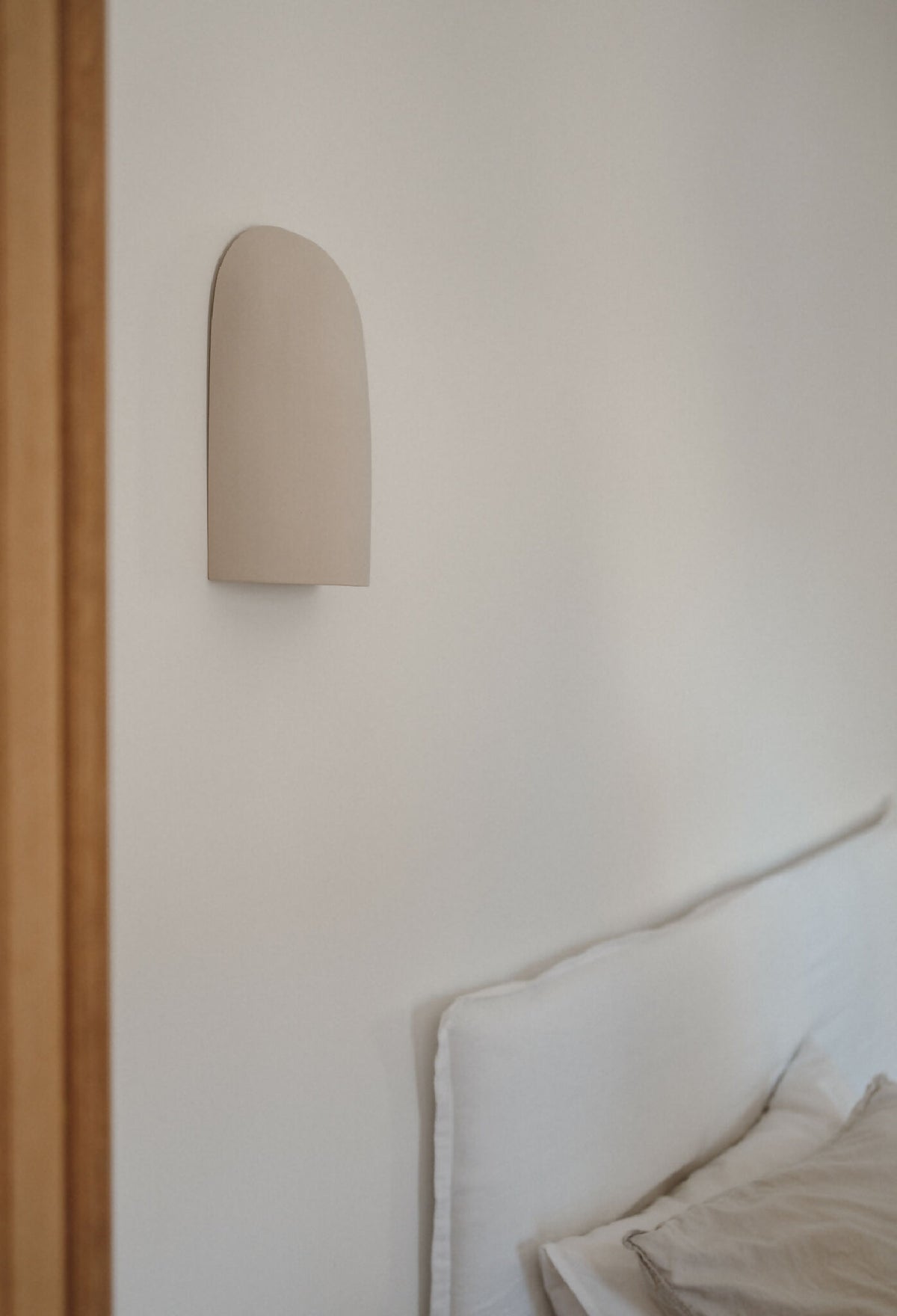 Applique murale beige en céramique sur mur, près d’un lit avec coussins.