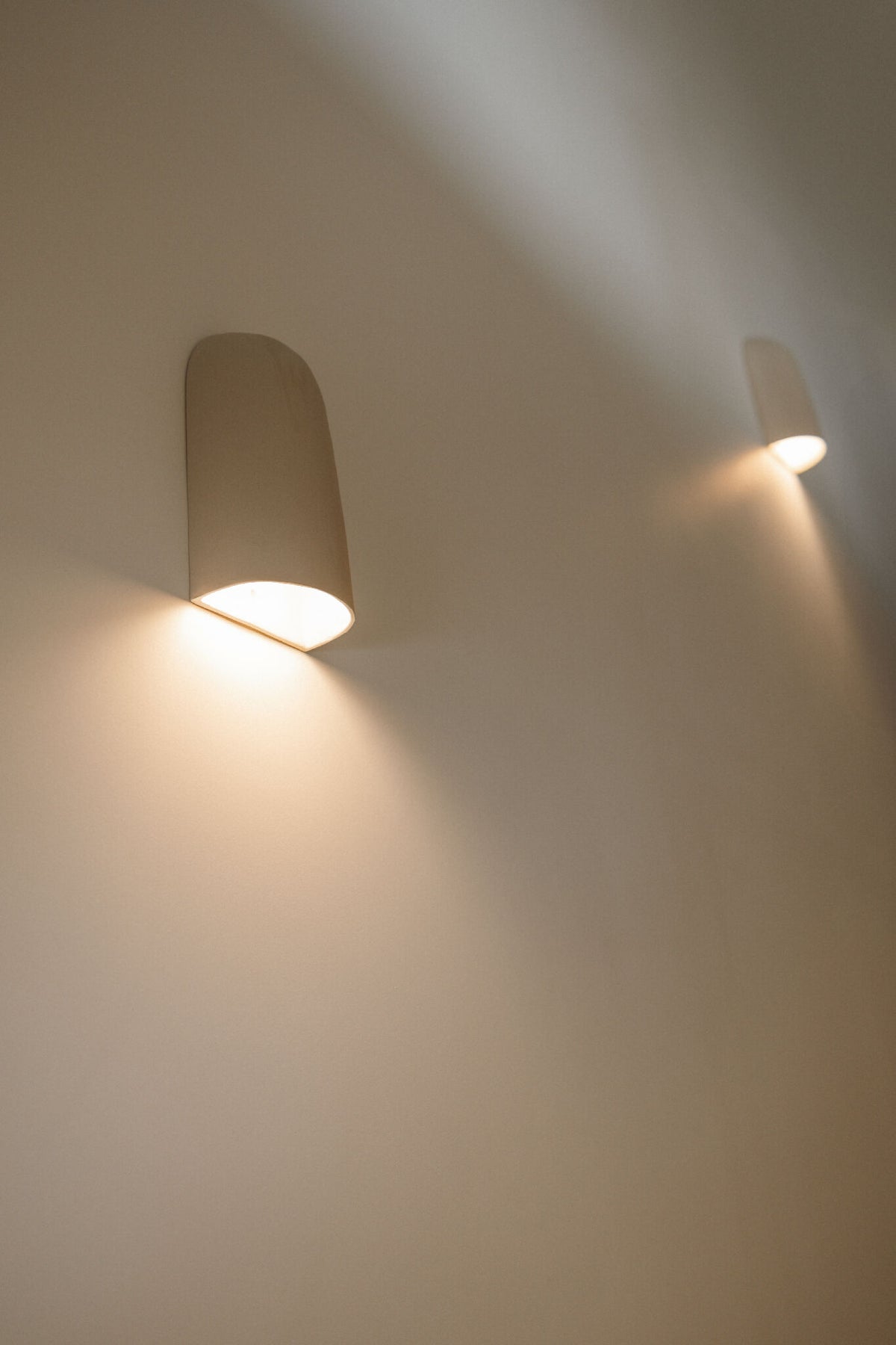 Applique murale en céramique beige, abat-jour arrondi, faisceau lumineux vers le mur.
