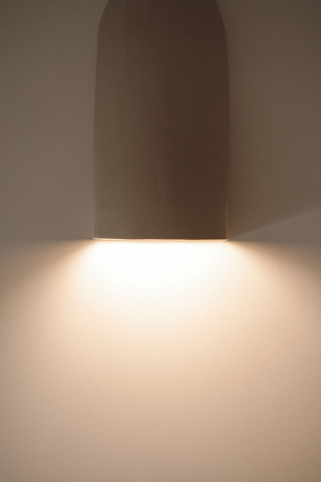Applique murale en céramique beige, abat-jour haut, lumière chaude vers le bas.