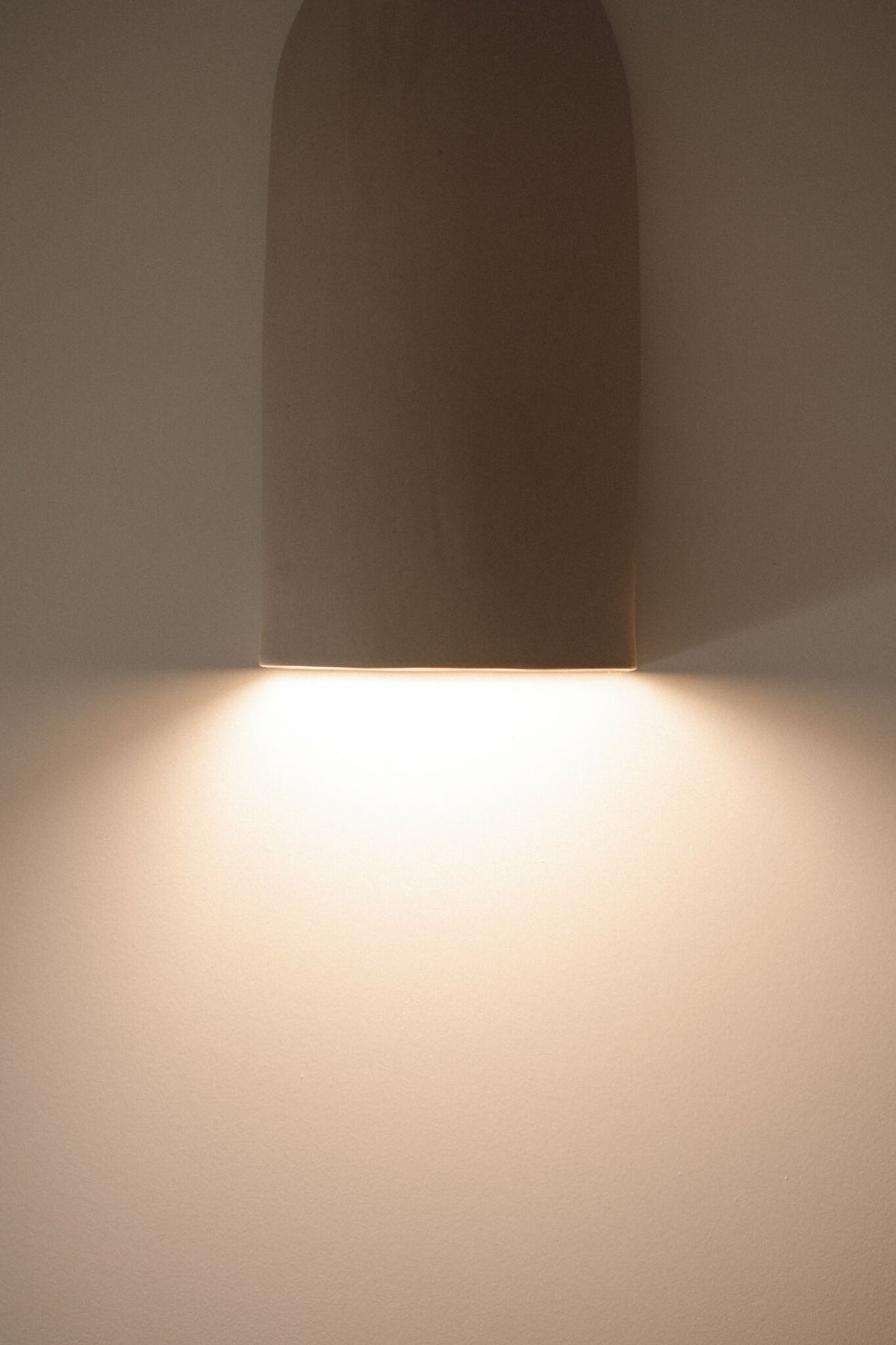 Applique murale en céramique beige, abat-jour haut, lumière chaude vers le bas.