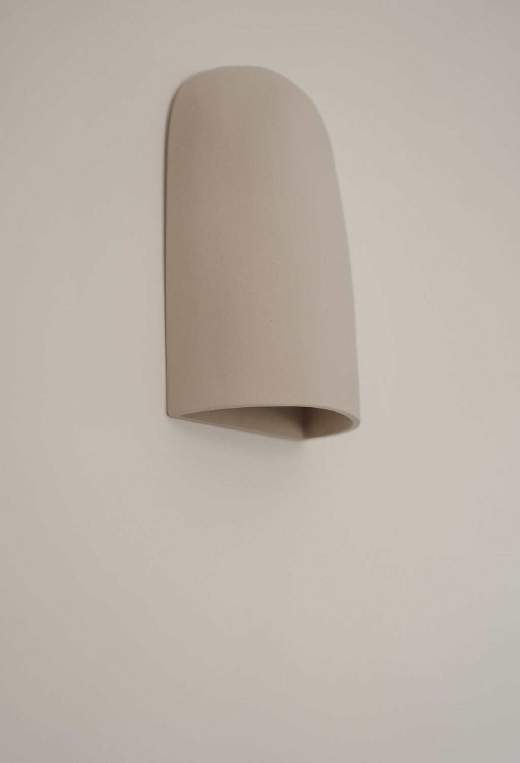 Applique murale beige en céramique, abat-jour courbé, angle légèrement décalé.