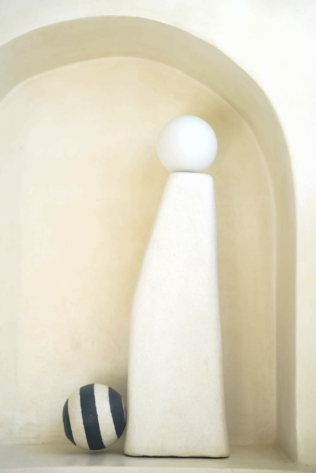 Sculpture lumineuse blanche dans une niche, sphère supérieure et boules rayées noir et blanc.