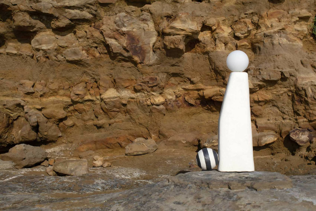 Sculpture lumineuse blanche sur rocher, sphère en haut et boule rayée sur le côté.