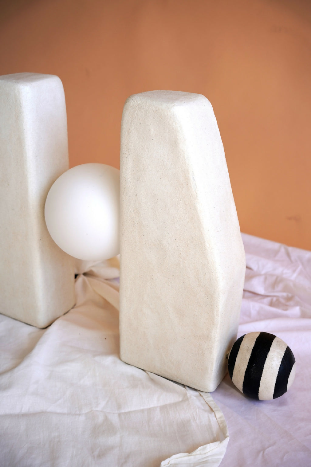 Sculpture lumineuse avec deux blocs rectangulaires crème et une sphère blanche.