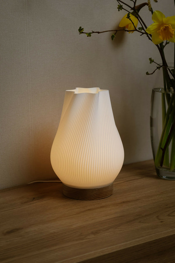 Lampe d’intérieur à abat-jour blanc côtelé, base en bois, lumière douce allumée.