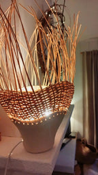 Luminaire conique en rotin brun tressé sur pot en grès, éclairage chaud allumé.