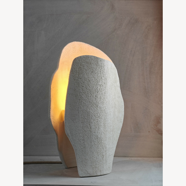 Sculpture lumineuse beige texturée, lumière chaude derrière la forme arrondie.