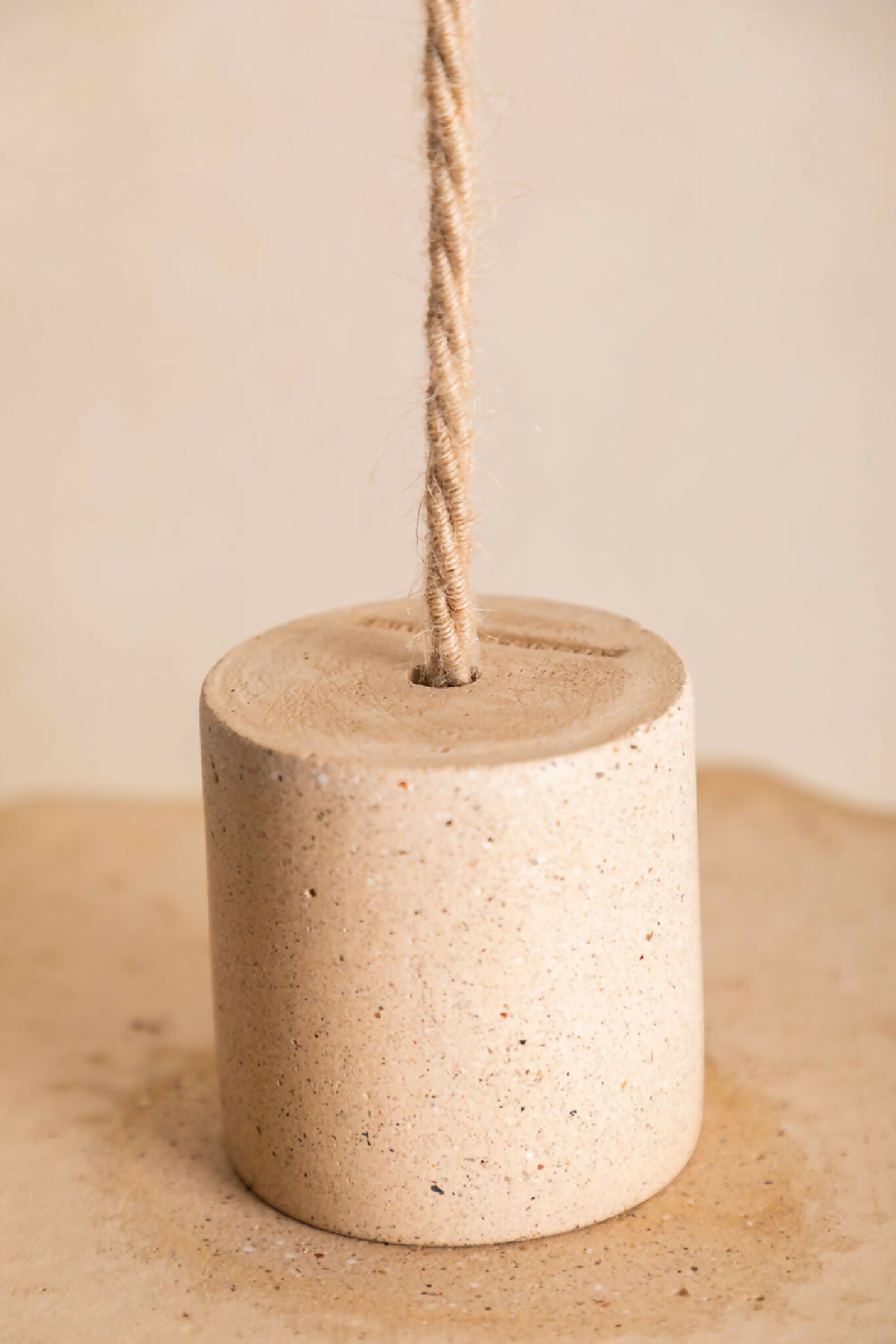 Cylindre suspendu en béton texturé beige avec cordon et capot supérieur assorti.