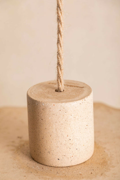 Cylindre suspendu en béton texturé beige avec cordon et capot supérieur assorti.