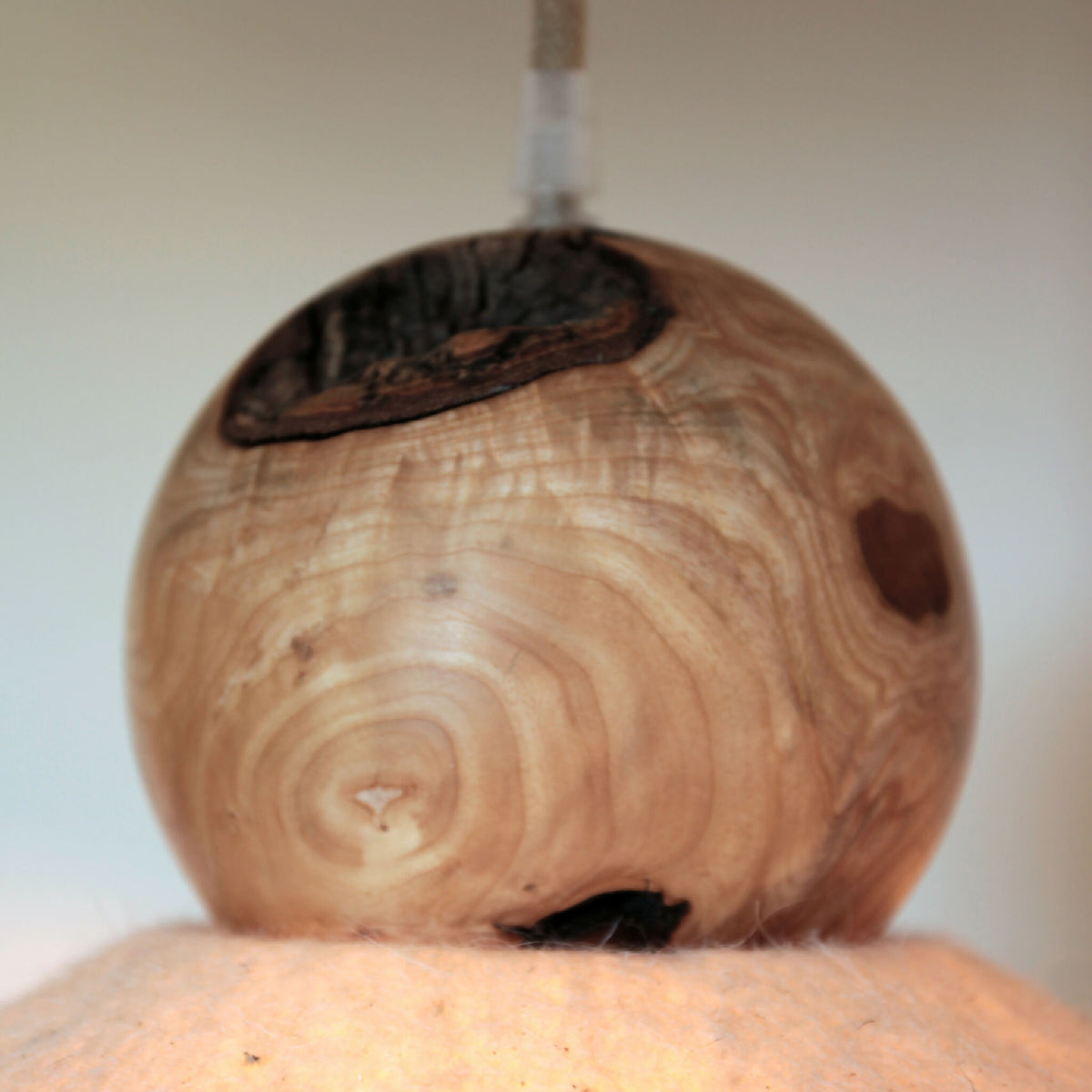 Sphère en bois sculpté avec capuchon en feutre sombre et fixation du câble.