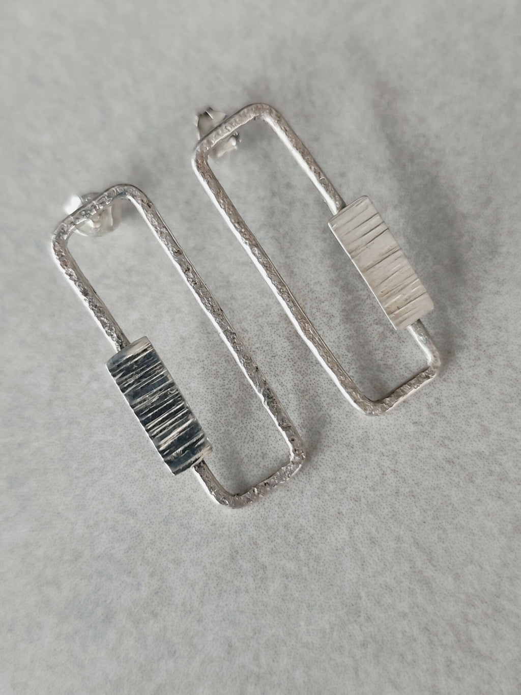 Boucles d’oreilles rectangulaires argentées, gros plan des textures à rayures.