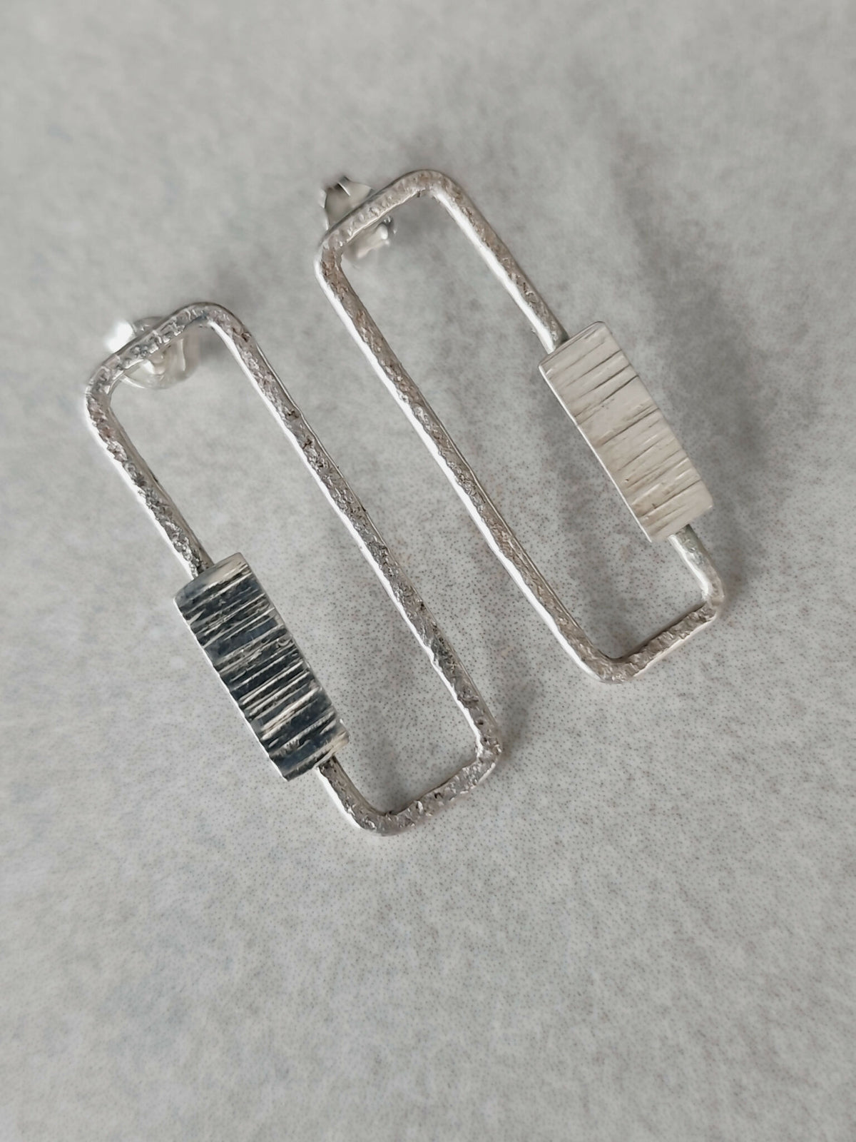 Boucles d’oreilles rectangulaires argentées, gros plan des textures à rayures.